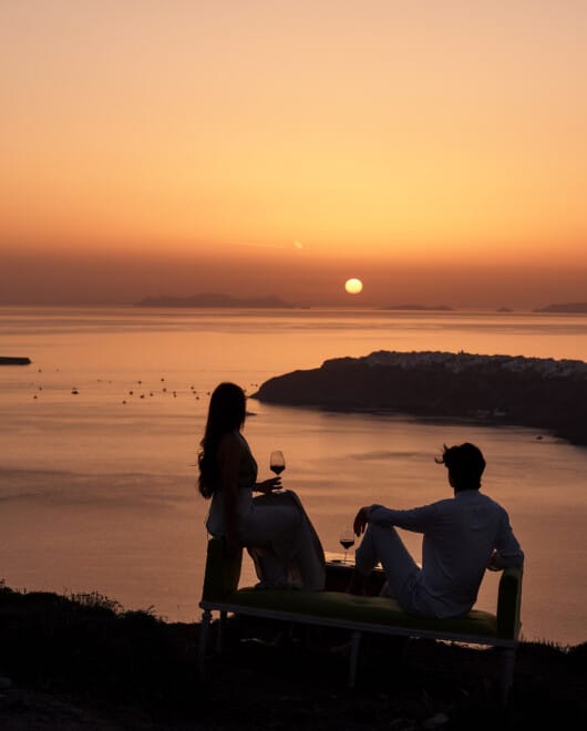 Couple enjoying a glass of wine to cap off their dinner at one of the best Santorini restaurants with a sunset view, at Andronis Hotels.