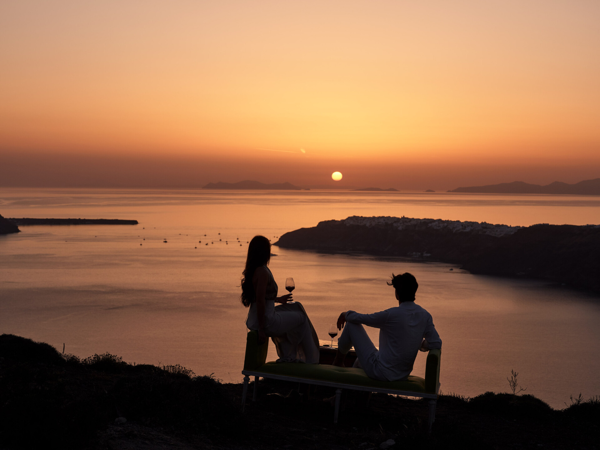 Couple enjoying a glass of wine to cap off their dinner at one of the best Santorini restaurants with a sunset view, at Andronis Hotels.